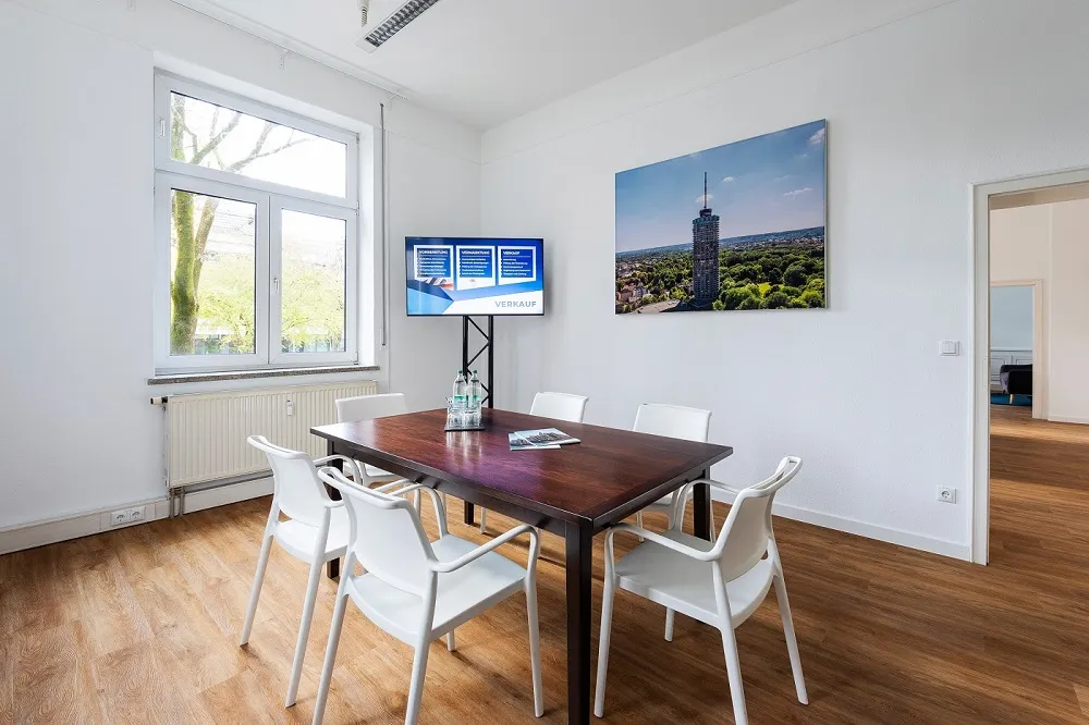 Der Besprechungsraum bietet eine professionelle Umgebung für Beratungsgespräche rund um den Immobilienverkauf, -kauf und die Immobilienbewertung in Augsburg. Die moderne Einrichtung, das helle Tageslicht und das Wandbild vom Hotelturm Augsburg vermitteln Seriosität, Transparenz und regionale Verbundenheit.